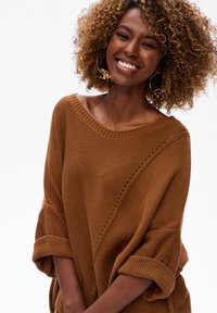 Brązowy, oversize sweter o luźnym kroju, szerokim dekolcie i podwiniętych mankietach. Posiada fakturowany wzór z ukośnymi liniami i wycięciami.