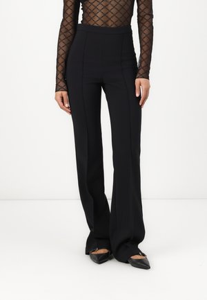 Black flared trousers in a structured fabric, featuring a high waist, clean lines, and a smooth texture. Paired with pointed black flats.