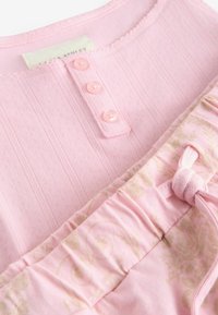 Tissu côtelé rose clair avec trois petits boutons et un tissu à motif floral rose assorti avec un nœud de cordon.