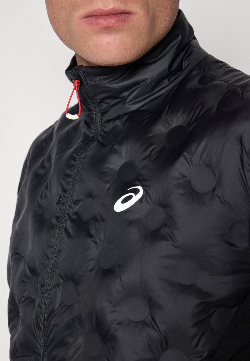 Chaqueta de plumas negra con patrones circulares texturizados, un cuello alto y una cremallera con un tirador rojo. Presenta un logo blanco en el pecho.