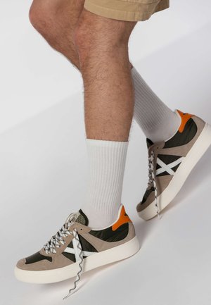 Sneakers realizzati in materiali scamosciati e tessili, con dettagli beige, verde oliva e arancio, suole bianche e lacci a zig zag.