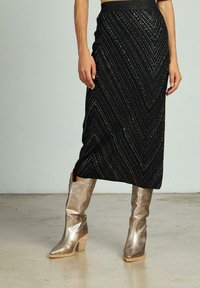 Jupe en tricot noir avec un motif en chevrons et un fil métallique, associée à des bottes de cow-boy dorées brillantes avec un talon bloc et une couture décorative.