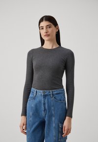 Maglione grigio a maniche lunghe in tessuto a costine abbinato a pantaloni cargo in denim blu a vita alta, con tasche laterali e chiusura con bottone.