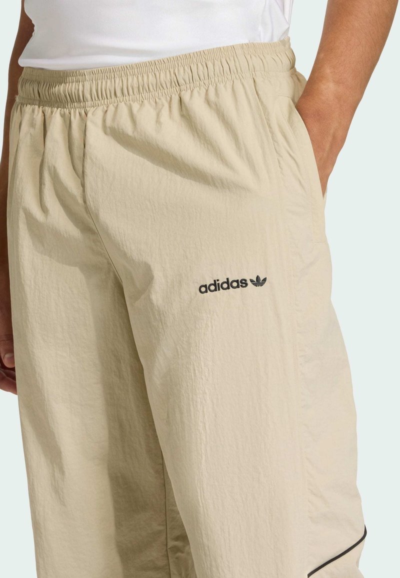 Pantaloncini beige leggeri con vita elastica, tasche laterali e logo Adidas nero sulla coscia sinistra. Tessuto strutturato, antimacchia.