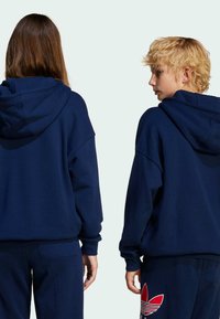 Sweatshirts bleu marine avec une coupe décontractée. Tissu doux avec ourlet et poignets côtelés. L'un présente un grand logo rouge Adidas au dos.