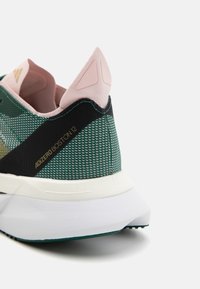 Zielono-czarny but do biegania z teksturowaną siateczkową cholewką, bladoróżowymi akcentami i białą podeszwą. Posiada oznaczenie „adizero Boston 12”.