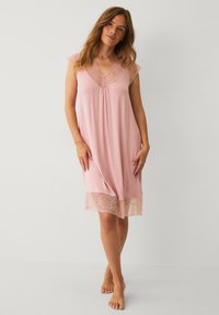 Helle rosa Nachthemd mit Spitze am Ausschnitt und Saum. Kurze Ärmel und lockere Passform. Weicher, glatter Stoff mit leichter Drapierung.