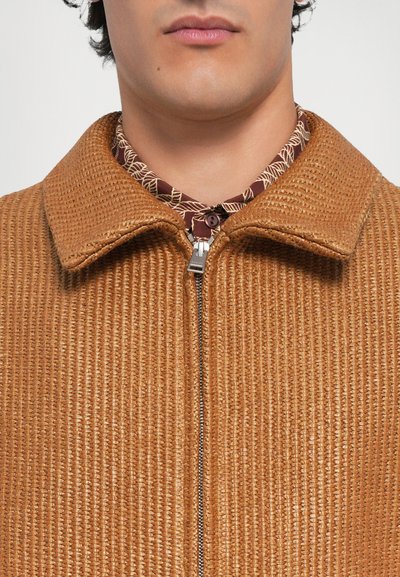 Chaqueta texturizada marrón con cierre de cremallera y cuello, superpuesta a una camisa estampada con un diseño en burdeos y crema.