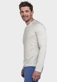 Hellgraues, langärmeliges, geripptes Performanceshirt mit Rundhalsausschnitt und nähtechnischen Akzenten, kombiniert mit blauen Hosen. Keine sichtbaren Logos.