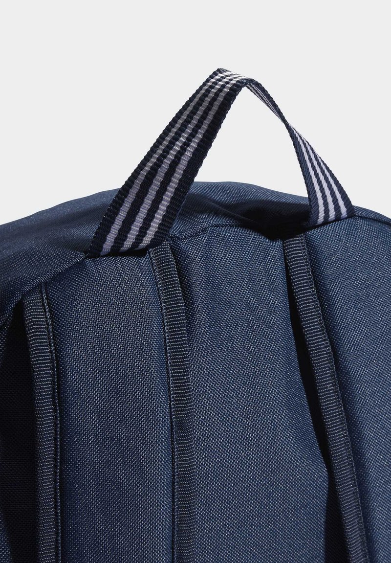 Zaino blu navy con tessuto a trama, dotato di manico a strisce e dettagli di cucitura lungo i lati. Vista dall'alto che mostra la forma e il materiale.