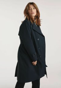 Granatowy płaszcz trench z podwójnym zapięciem, dużymi klapami i zapięciami na guziki. Charakteryzuje się dopasowanym krojem i bocznymi kieszeniami.