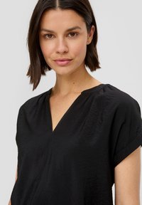Schwarzes, kurzärmliges Oberteil mit V-Ausschnitt, weichem Stoff und minimalistischem Design, mit dezenten Falten an den Schultern.