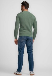 Maglione verde lavorato a maglia con texture a costine e scollatura rotonda, abbinato a jeans blu e sneakers bianche con dettagli neri.