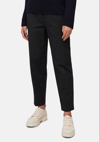 Persoon in zwarte rechte broek en off-white stevige veterschoenen, staand tegen een effen lichte achtergrond.
