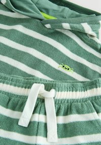 Zöld-fehér csíkos melegítőszett, puha frottír anyagból, kapucnis felsővel és egy kis hímzett rák motívummal a mellkason.