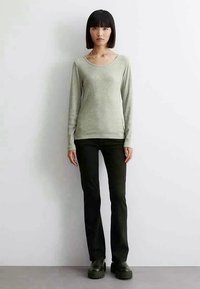 Light green long-sleeve top with a scoop neckline, paired with black fitted pants and chunky black boots, set against a plain background.