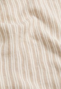 Tejido textil con una textura ondulada que presenta franjas alternas en beige y blanco, creando un patrón sutil a través de la superficie.