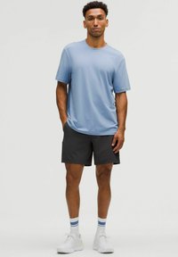 Lyseblå kortærmet t-shirt, sorte shorts, hvide sneakers og stribede sokker; afslappet pasform og glat stoftekstur.