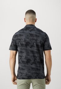 Tričko s krátkým rukávem z tmavě šedé látky s texturovaným vzorem, které má černé akcenty, tradiční límec a volný střih.