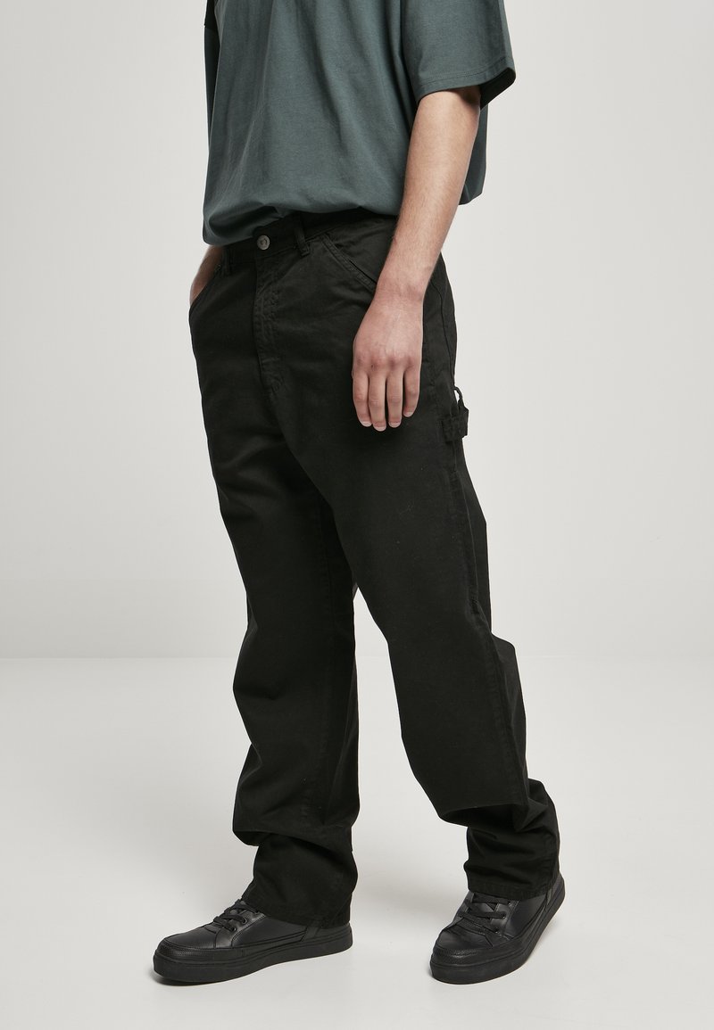 Svart cargo-bukser med løs passform, med sidelommer og teksturert stoff. Kombinert med svarte joggesko og en grå oversized T-skjorte.