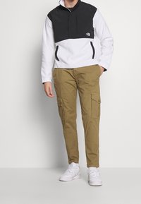 Zwart-wit fleece met een halve rits, gecombineerd met kaki cargobroek met zijzakken en witte sneakers.