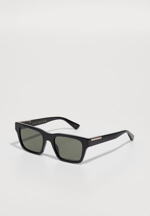 Gafas de sol rectangulares negras con lentes verdes. Cuentan con un acento metálico en las patillas y un logo grabado en dorado. Acabado texturizado.
