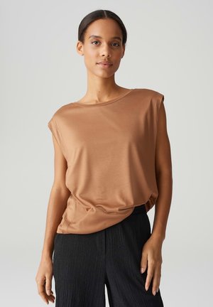 Brown, short-sleeve top made from a smooth material, featuring a loose fit and round neckline, paired with textured black pants.