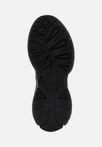 Sole di scarpa sportiva nera con motivi texture, inclusi solchi e forme per la trazione, dotata di un'area centrale liscia.