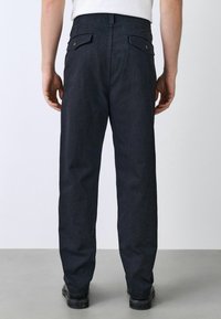 Dark denim trousers with a straight fit, featuring two back pockets and sturdy hardware. Subtle texture with a clean, minimalist design.