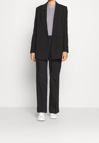 Blazer negro de doble botonadura, pantalones negros ajustados y zapatillas blancas. La camisa tiene un pequeño patrón, añadiendo contraste al atuendo.