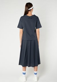 Abito blu navy con colletto ampio, maniche corte e gonna plissettata. Abbinato a sneakers bianche e calze a righe. Tessuto dalla texture liscia.