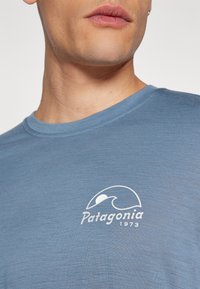 Blue short-sleeve t-shirt made of soft fabric, featuring a white Patagonia logo with a wave and the year 1973 near the neckline.