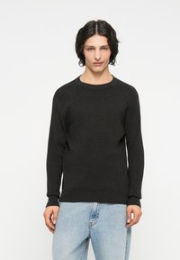 Dark gray ribbed sweater with long sleeves and a round neckline, paired with light blue jeans. The texture is soft and knitted.