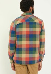 Karierte Multicolor-Hemden mit roten, grünen, blauen und gelben Quadraten; mit Knopfmanschetten und einem Schulterdetail auf der Rückseite. Baumwollstoff.