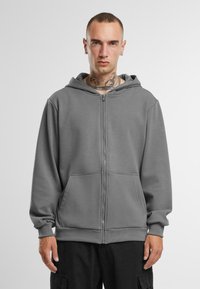 Grå zip-hoodie i blødt materiale med frontlynlås, to store lommer og hætte med snøre. Har ribbede manchetter og kant.