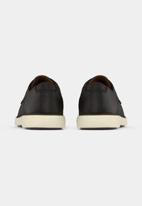 Chaussures en cuir noir avec une coupe basse, une forme arrondie, une semelle en caoutchouc blanche contrastante et un détail de couture minimal au niveau du talon.