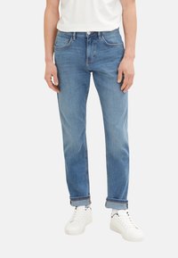 Jeans din denim de culoare albastru deschis, cu o croială dreaptă, ușor decolorate și un design clasic cu cinci buzunare, asortați cu adidași albi.