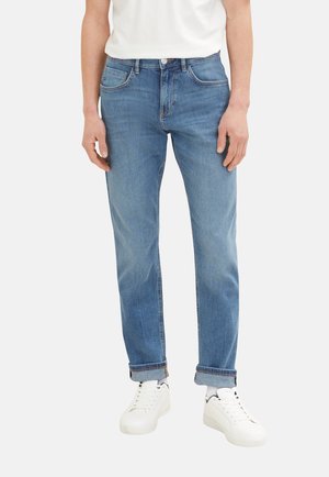 Helle blaue Jeans im klassischen Schnitt mit subtilen Used-Effekten und klassischem Fünf-Taschen-Design, kombiniert mit weißen Sneakern.