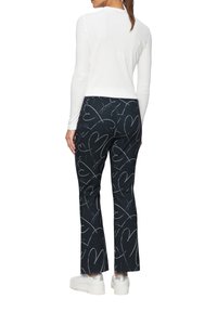 Witte longsleeve top gecombineerd met donkerblauwe broek met een hartpatroon en witte krabbels. Model draagt witte sneakers.