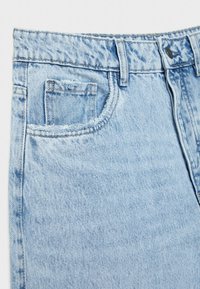 Vaqueros de mezclilla azul claro con una textura desgastada, un pequeño bolsillo frontal y cierre de cintura estándar. El dobladillo superior muestra bordes deshilachados.