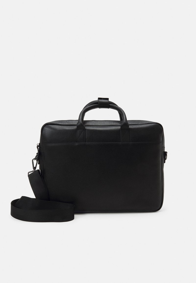 Malette en cuir noire avec deux poignées supérieures, une bandoulière amovible et une texture lisse. Présente un design minimaliste sans marquage visible.