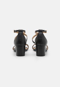 Sandales à talons en cuir noir avec un dos fermé, une sangle de cheville avec boucle et un design découpé sur les côtés. Talon en bloc épais.