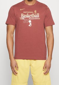 Punainen puuvillapaita, jossa on kultainen NBA-logo, teksti "Kansallinen Koripallojoukkue 31" ja palkkigraphiikka edessä. Lyhyet hihat, klassinen malli.