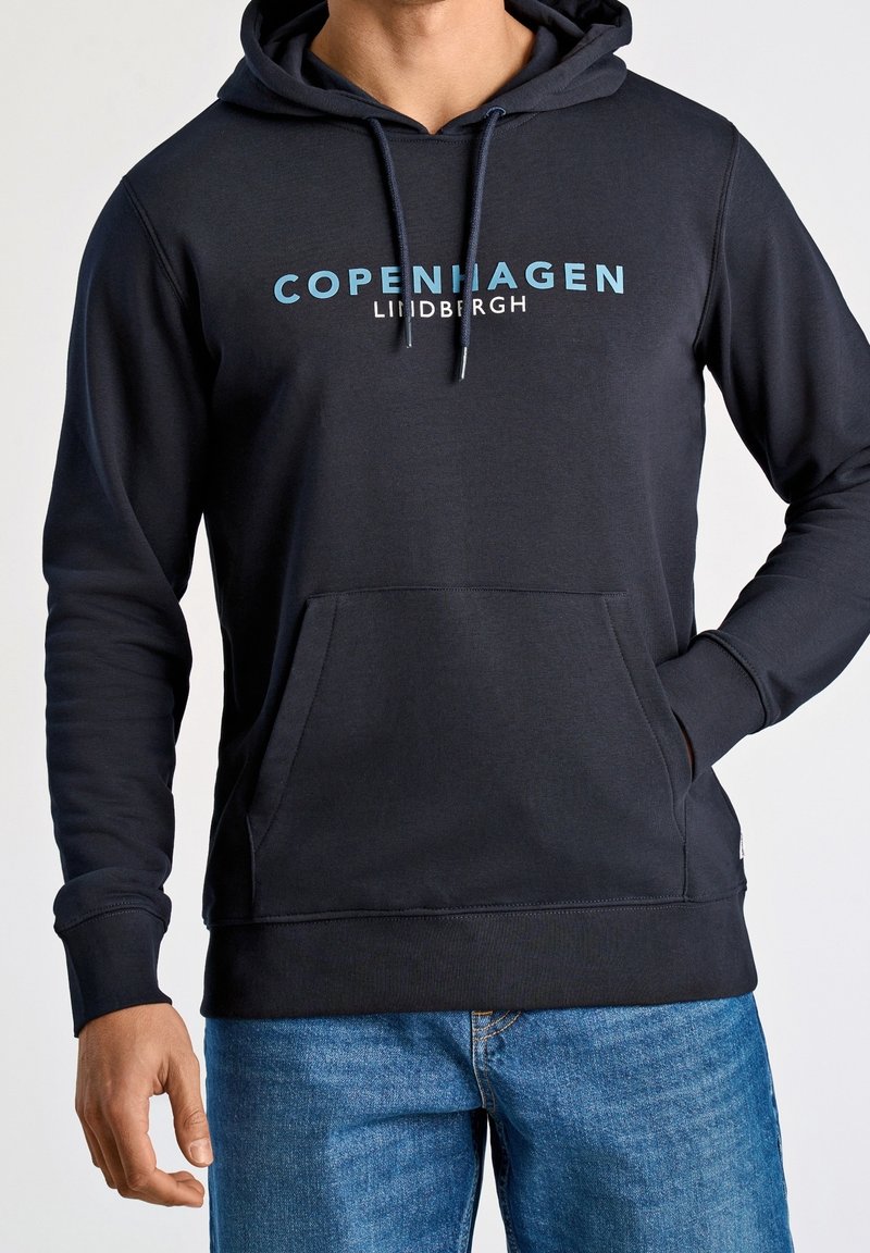 Tmavě modrá mikina s kapucí a přední kapsou, na které je nápis "COPENHAGEN" a "LINDBERGH" vytištěný světle modrou a bílou barvou.