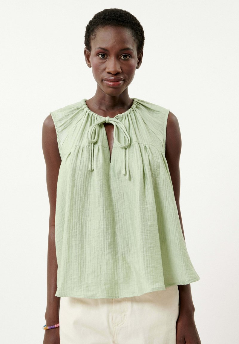 Blouse sans manches vert clair avec un col froncé, un détail de nœud à l'avant et une coupe décontractée. Tissu doux et texturé ; design décontracté.