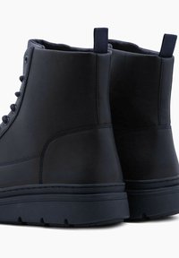 Botas de color azul marino oscuro, fabricadas con un material sintético suave, que presentan un diseño elegante, suela robusta y talón reforzado con un tirador.