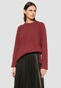Pull en tricot bordeaux avec un ourlet et des poignets côtelés, associé à une jupe plissée en simili cuir noir, dotée d'une coupe décontractée et de manches raglan.