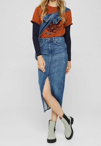 Džínová sukně s předním rozparkem, spárovaná s oranžovým tričkem s černým grafickým potiskem, vrstvená přes dlouhý rukáv námořnického topu.