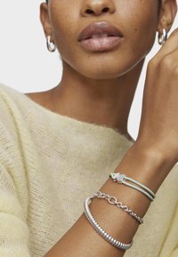 Pulseras en tono plata con diferentes texturas: una cadena pulida, un diseño de cuentas lisas y un cordón azul suave con un pequeño acento en plata.