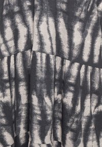 Vestido em camadas preto e creme com padrão tie-dye, textura de tecido suave e pregas horizontais. Foco no contraste de cores único e no design.